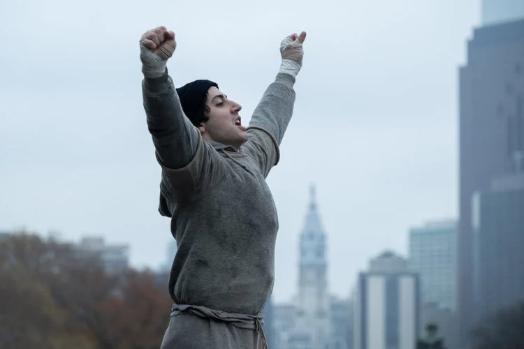 Anthony Ippolito como Sylvester Stallone, erguendo os braços em cena de Eu Sou o Rocky